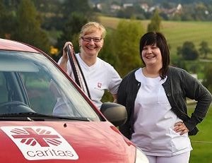 Zwei Caritas-Mitarbeitende vor einem roten Caritas-Auto.